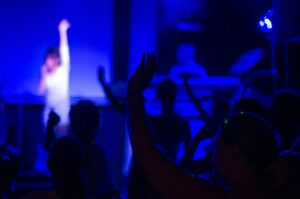 A dynamic nightclub scene with a live performance, vibrant crowd, and blue ambient lighting.